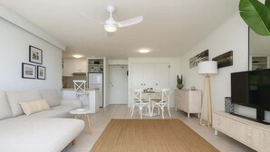 A modern living room with a sofa, a dining table with chairs, a TV, and a ceiling fan. - Ocean View 1BR Steps to Beach (Surfers Paradise)