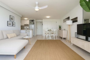 A modern living room with a sofa, a dining table with chairs, a TV, and a ceiling fan. - Ocean View 1BR Steps to Beach (Surfers Paradise)