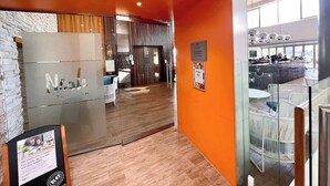Un interno moderno con pavimento in legno, pareti arancioni, una reception e un’area salotto con vista sulla città.