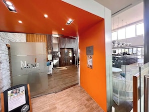 Ein modernes Interieur mit Holzboden, orangefarbenen Wänden, einem Empfangsbereich und einer Sitzecke mit Blick auf die Stadt.