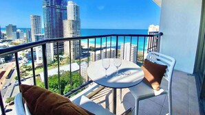 Un balcone con tavolo e sedie, affaccia su una vista che comprende sia il paesaggio urbano che la spiaggia.