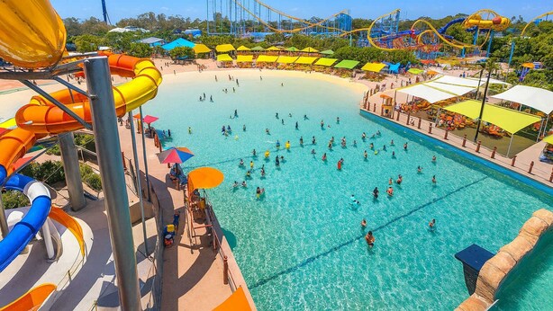Un parco acquatico con una grande piscina, scivoli d'acqua e un roller coaster sullo sfondo.