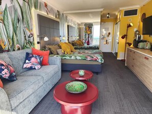 A room with a sofa, two red side tables, a bed with a floral bedspread, and a yellow wall. - Top Ocean View Artistic Apt (Surfers Paradise)