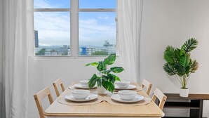 A dining table with white plates and bowls, a potted plant, and a view of the city through a window.