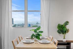 A dining table with white plates and bowls, a potted plant, and a view of the city through a window. - High-Rise Condado Suite | Ocean Views & PR Skyline (San Juan)