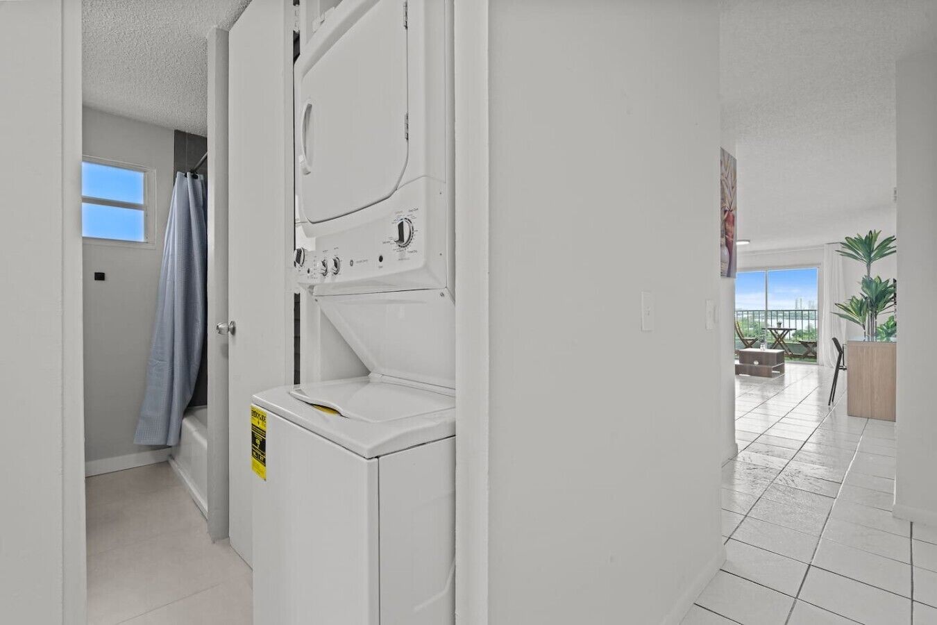 A laundry room with a washing machine and dryer, a shower area, and a view of a balcony with outdoor furniture.
