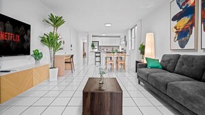 A modern living room with a TV, sofa, coffee table, and a dining area with chairs and a table.