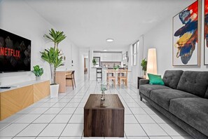 A modern living room with a TV, sofa, coffee table, and a dining area with chairs and a table. - High-Rise Condado Suite | Ocean Views & PR Skyline (San Juan)