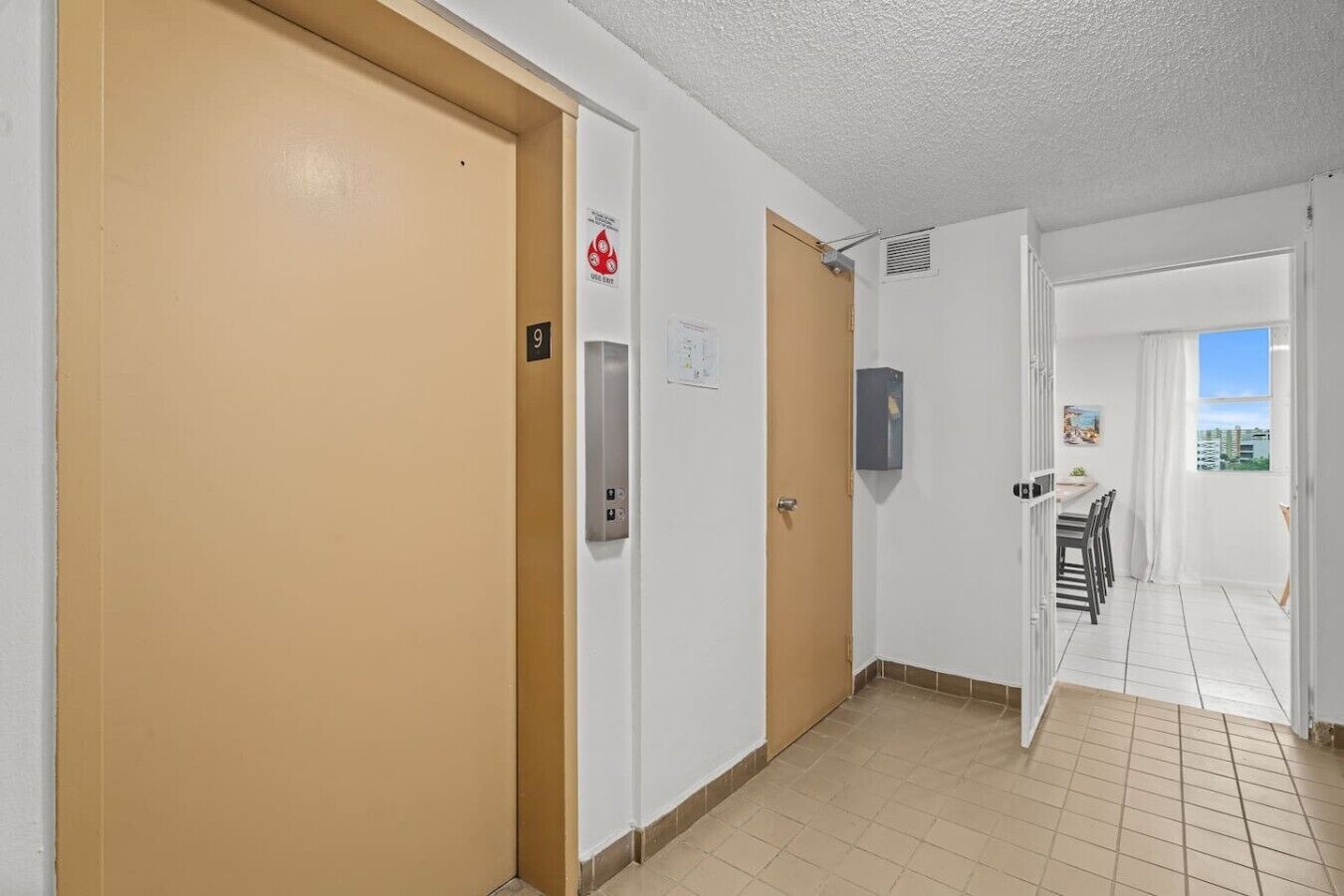 Un pasillo con puertas color beige, un letrero de salida de incendios, una unidad de ventilación y un comedor con vistas.