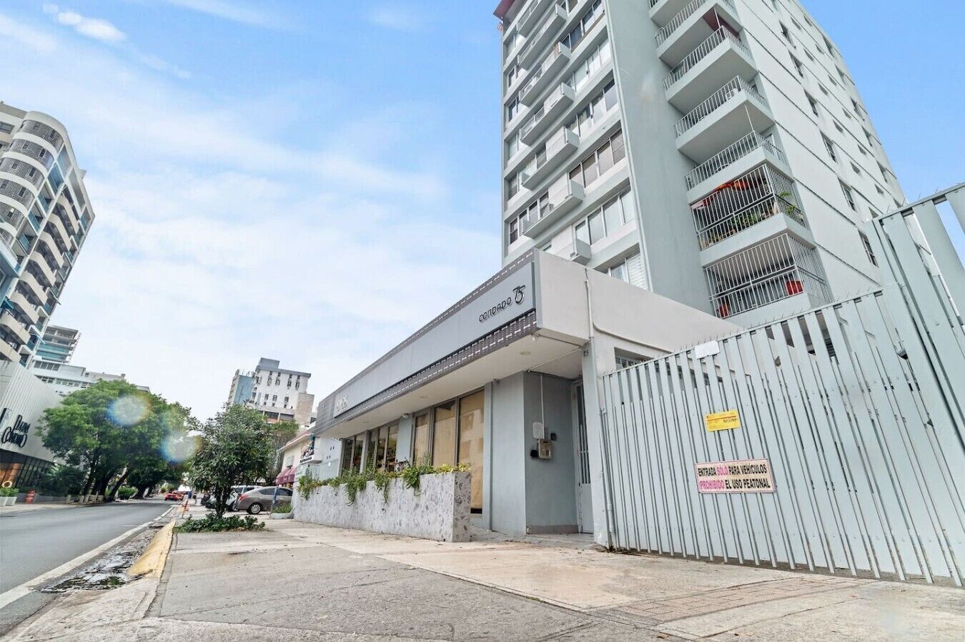 A modern building with a gated entrance, a sign indicating a parking area for vehicles, and a clear sky.