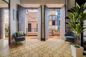 Ein offener Innenraum mit Fliesenboden, zwei Stühle, einem Blumentopf und Blick auf ein Gebäude mit Balkon.
