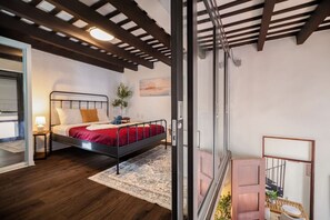 Ein Schlafzimmer mit Bett, Nachttisch, Lampe und Blick durch eine Glastür auf einen Balkon.