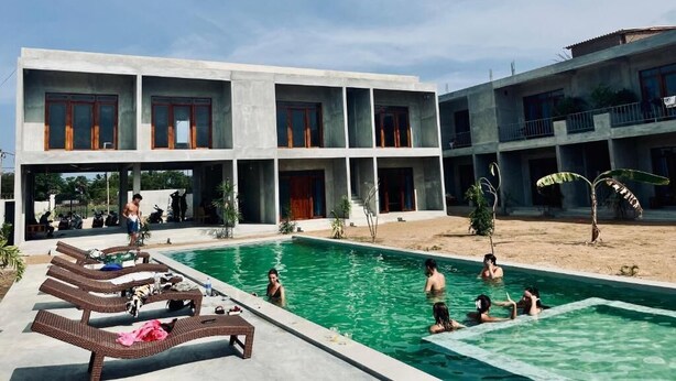 Zona de piscina con sillones de descanso y un edificio con varios balcones.