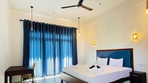 Habitación de hotel con cama, escritorio, silla, ventilador de techo y ventana con cortinas.