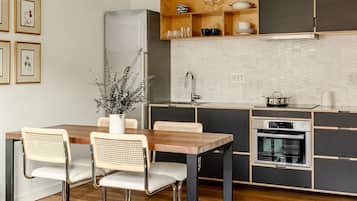 A modern kitchen with a wooden dining table, two wicker chairs, a built-in oven, and a stainless steel refrigerator.