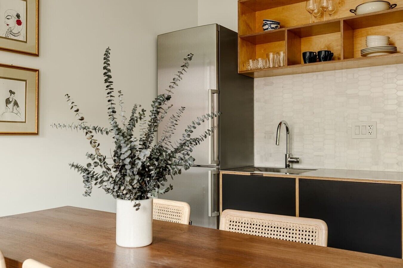A modern kitchen with a wooden dining table, a potted plant, and a built-in oven.
