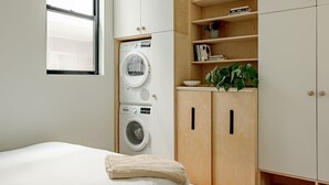 A bedroom with a bed, a washing machine, wooden cabinets, and a window.