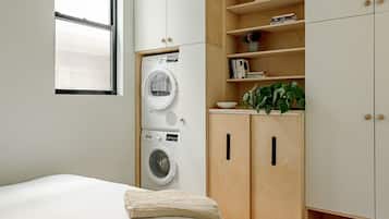 A bedroom with a bed, a washing machine, wooden cabinets, and a window.