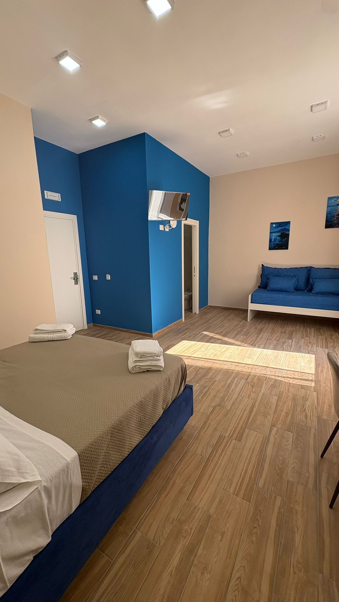 A hotel room with a bed, a sofa, a bathroom, and a blue wall.