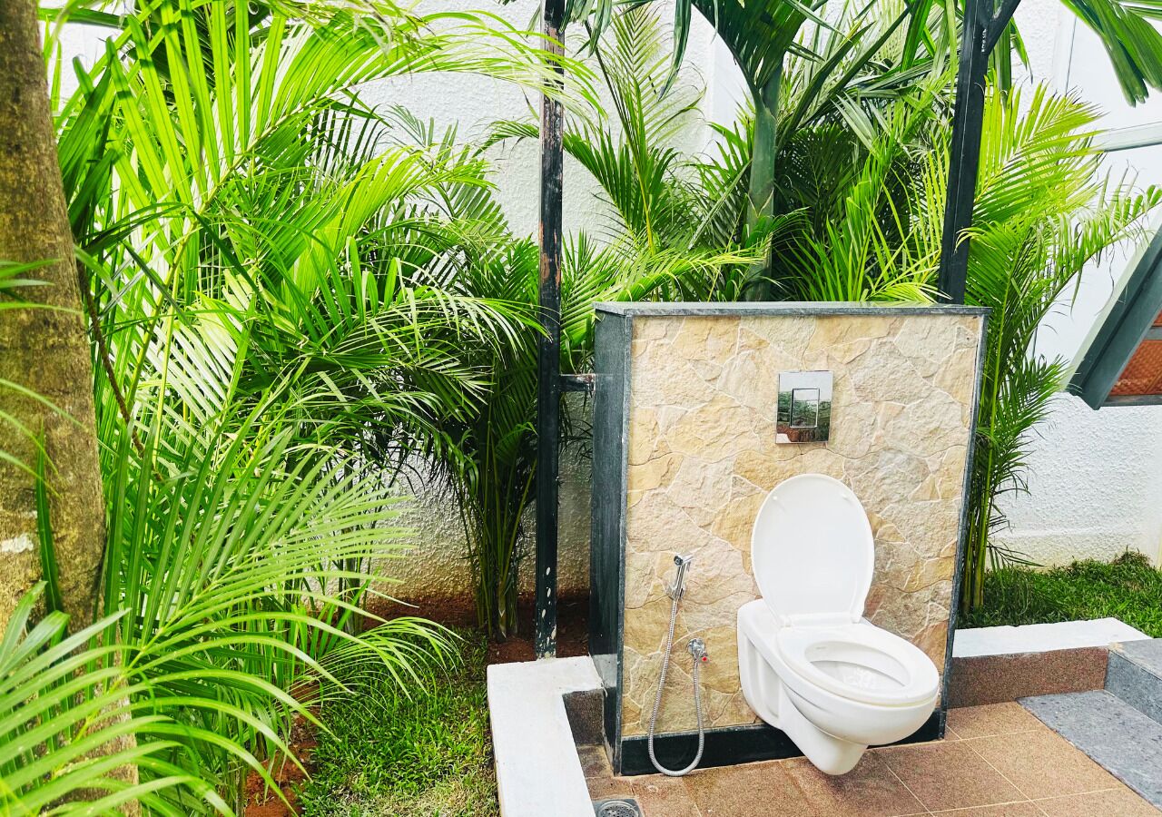 A portable outdoor toilet with a stone exterior, surrounded by lush greenery.