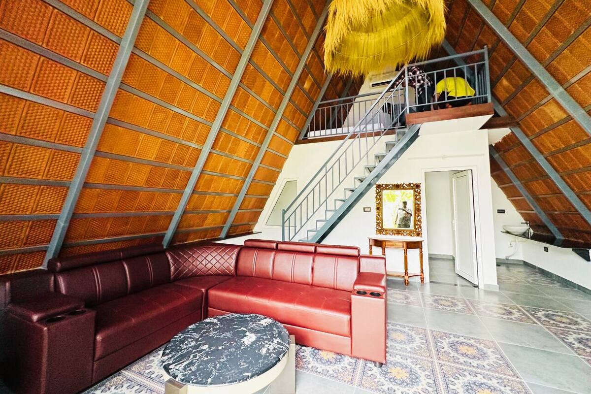 Una habitación amplia con un sofá de cuero rojo, una mesa redonda y una escalera que sube a un nivel superior.