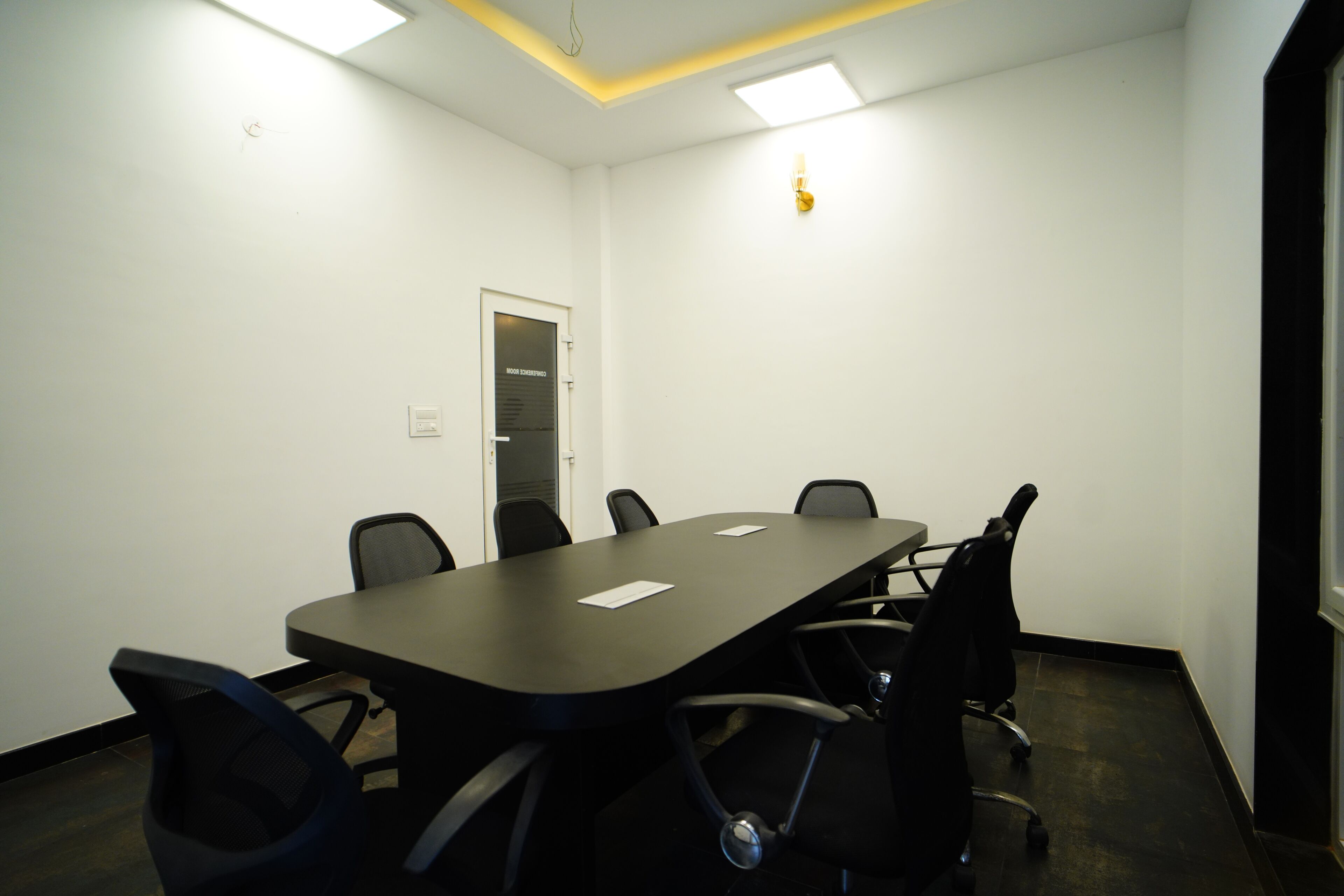 Una sala de conferencias con una larga mesa, seis sillas y una puerta con la leyenda 'Conference Room'.