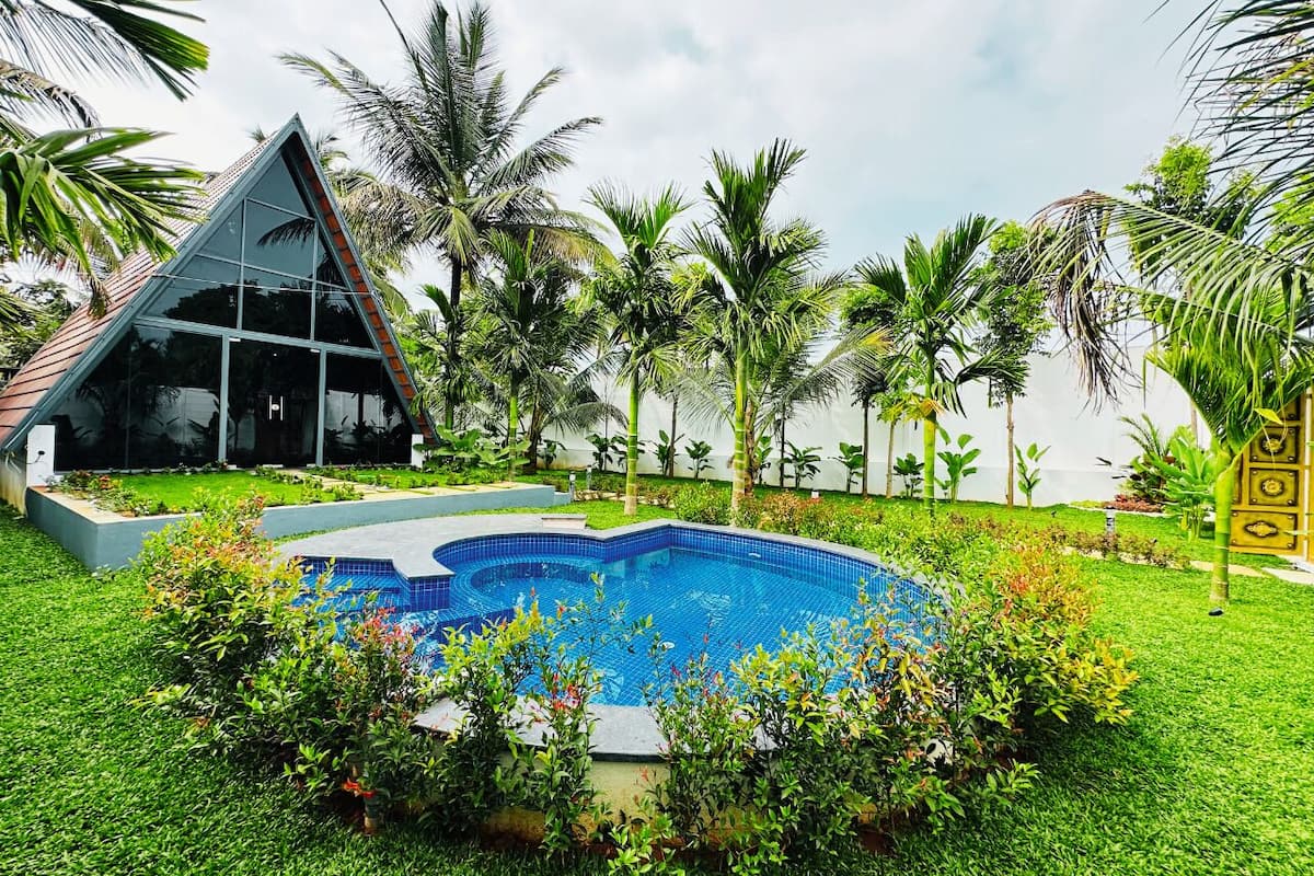 A swimming pool surrounded by lush greenery, a triangular glass building, and palm trees.