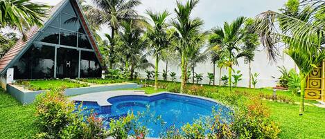 A swimming pool surrounded by lush greenery, a triangular glass building, and palm trees.