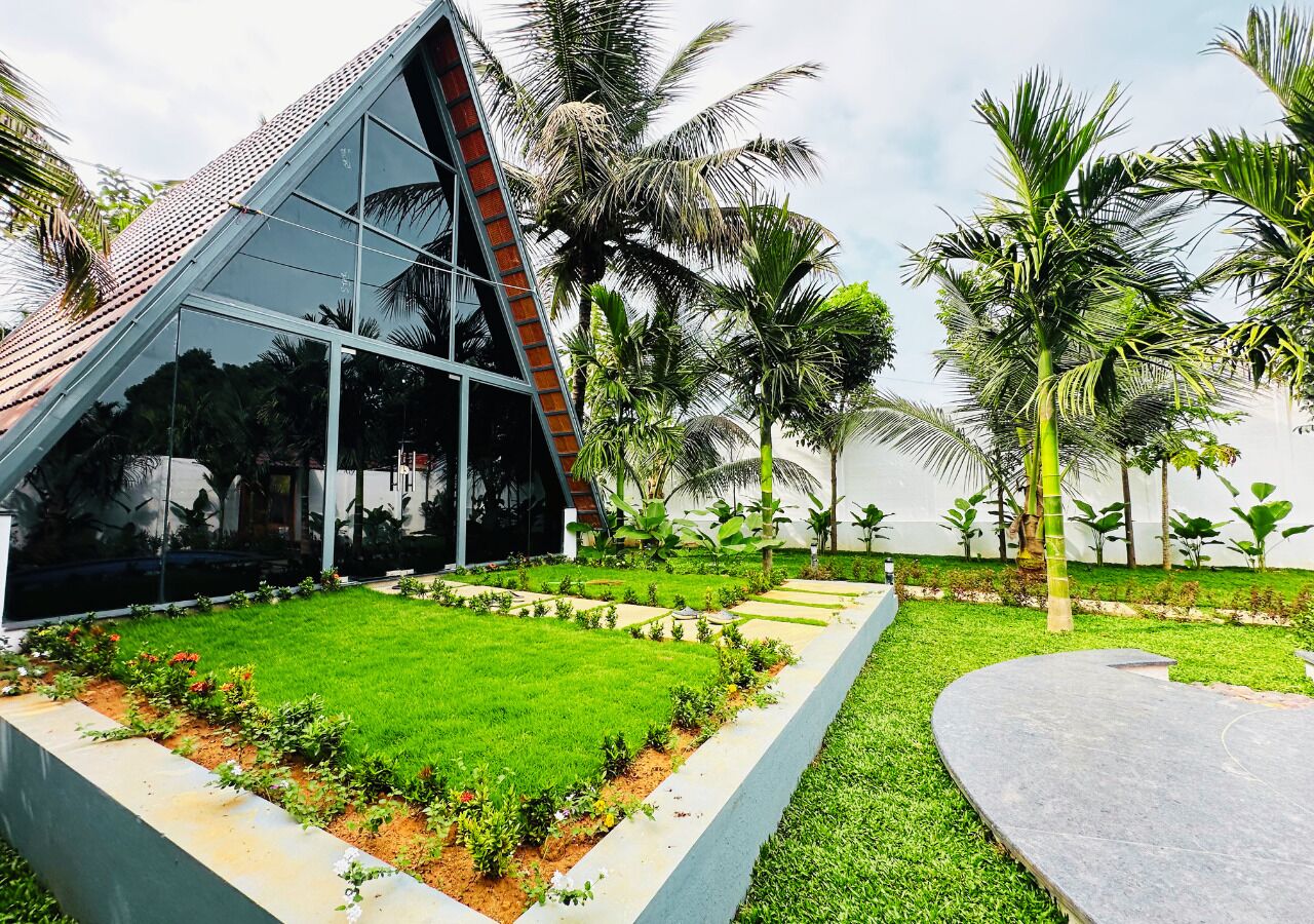 A modern building with a glass facade, surrounded by a well-maintained garden with palm trees and a clear sky.