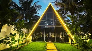Un edificio moderno con fachada triangular de vidrio, rodeado de exuberante vegetación y un césped bien cuidado.