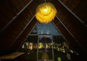 A room with a large glass window, a hanging light fixture, and a view of the outdoors.