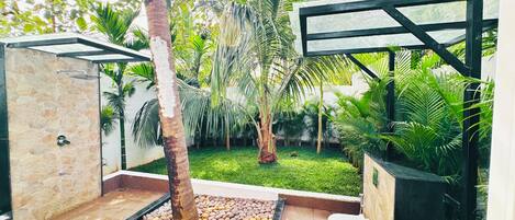Un baño al aire libre moderno con pared de piedra, una palmera y suelo de baldosas.
