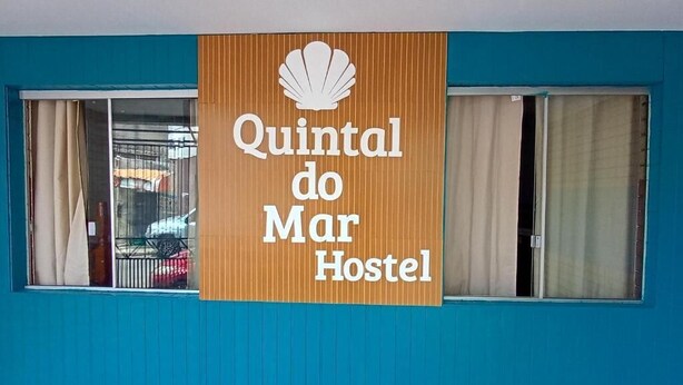 A hostel sign with a shell logo and the name 'Quintal do Mar Hostel' on a blue wall. - Quintal do Mar Hostel (Salvador)