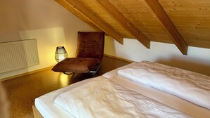 Une chambre avec un lit simple, un fauteuil à bascule, un radiateur et un plafond en pente.