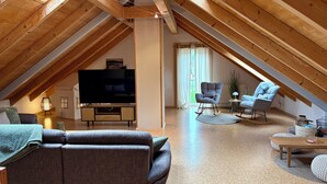 Un salon chaleureux aménagé dans les combles, avec un téléviseur, des canapés et un coin repas.
