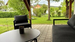 Une terrasse extérieure avec une table et deux chaises, entourée de verdure et offrant une vue sur des maisons au loin.