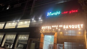 En hotellentréd med en skylt som visar ”Hotel Maple Inn & Banquet” och en neonreklamskylt ovanför.