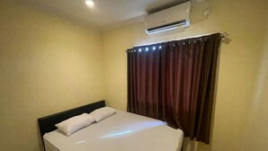 A single bed with white bedding, a headboard, and a wall-mounted air conditioner. - Cozzy Galaxy Hotel (Manado)