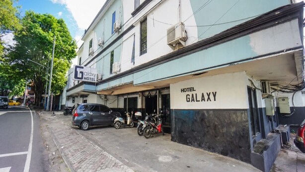 A building with a sign reading 'HOTEL GALAXY' and a covered parking area with motorcycles. - Cozzy Galaxy Hotel (Manado)