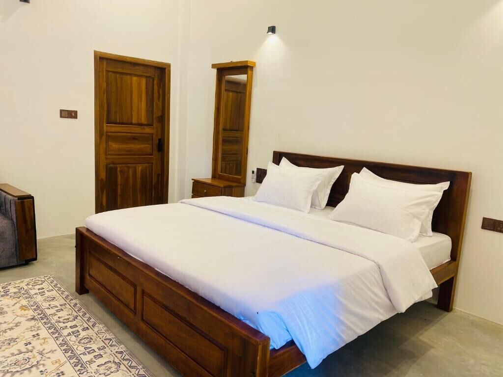 Un dormitorio con cama de madera, ropa de cama blanca, una mesita de noche, un espejo y una alfombra estampada.
