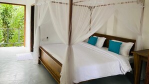 Una cama con dosel con ropa de cama blanca, almohadas azules, un cabecero de madera y vistas al follaje a través de una puerta abierta.