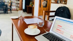 Una mesa de madera con una computadora portátil, una taza de café y un vaso de agua.