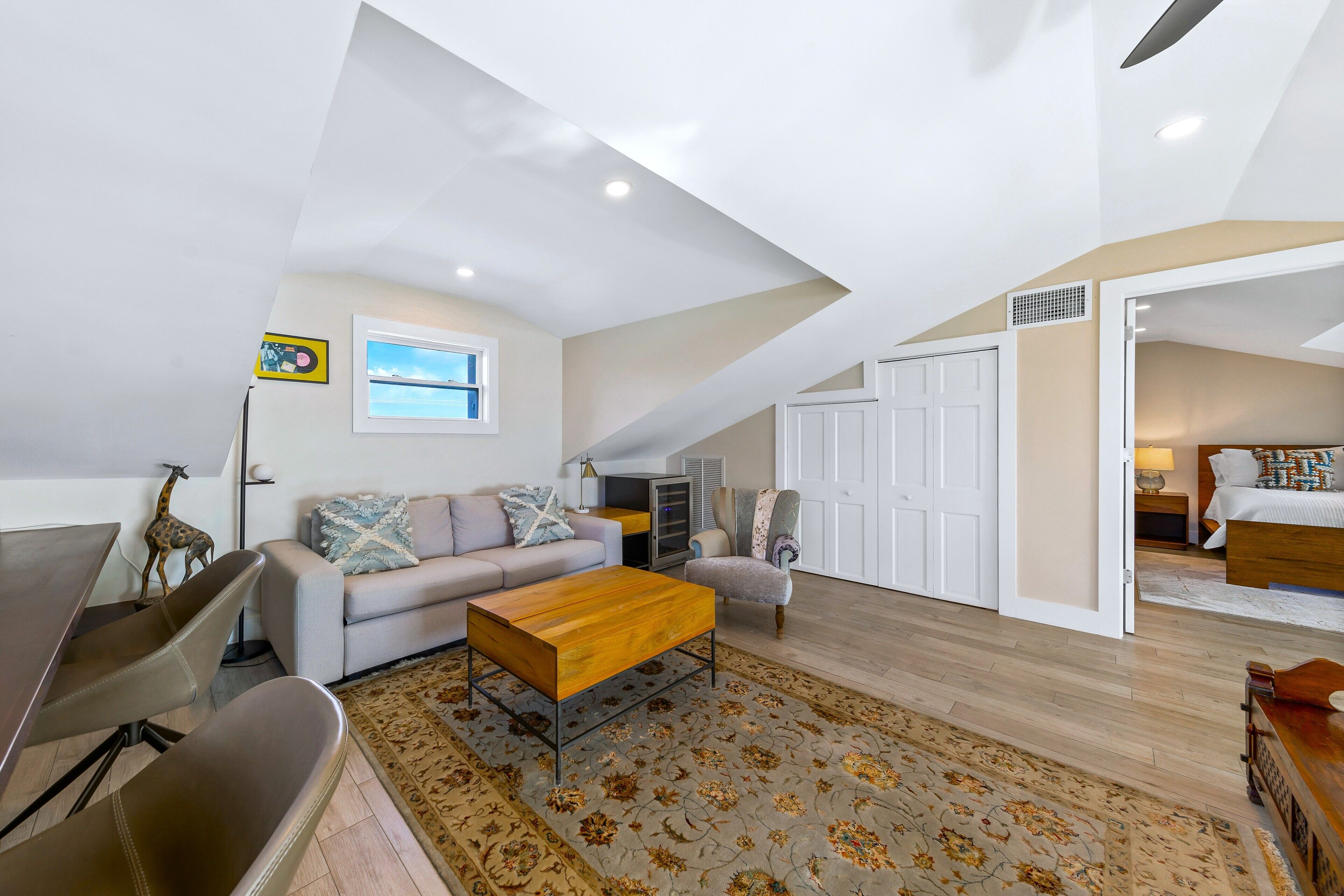 Un loft espacioso con techo alto, zona de comedor con mesa de madera, sofá y alfombra estampada.