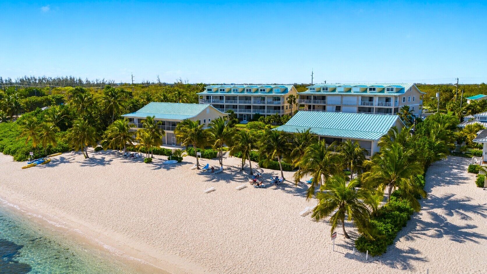 A beachfront hotel with multiple balconies, a sandy beach, and palm trees.
