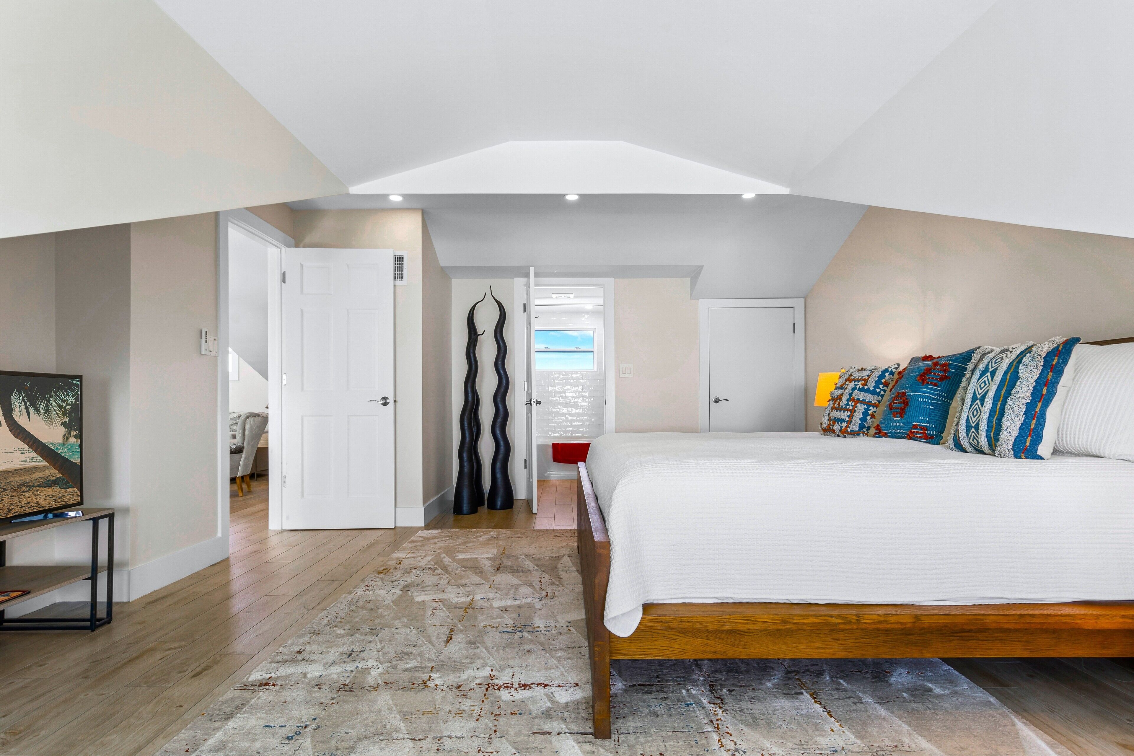A bedroom with a bed, a TV, and a view of the sky through a door.