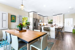 Una cocina moderna con armarios blancos, una isla central y un comedor con mesa y sillas de madera.