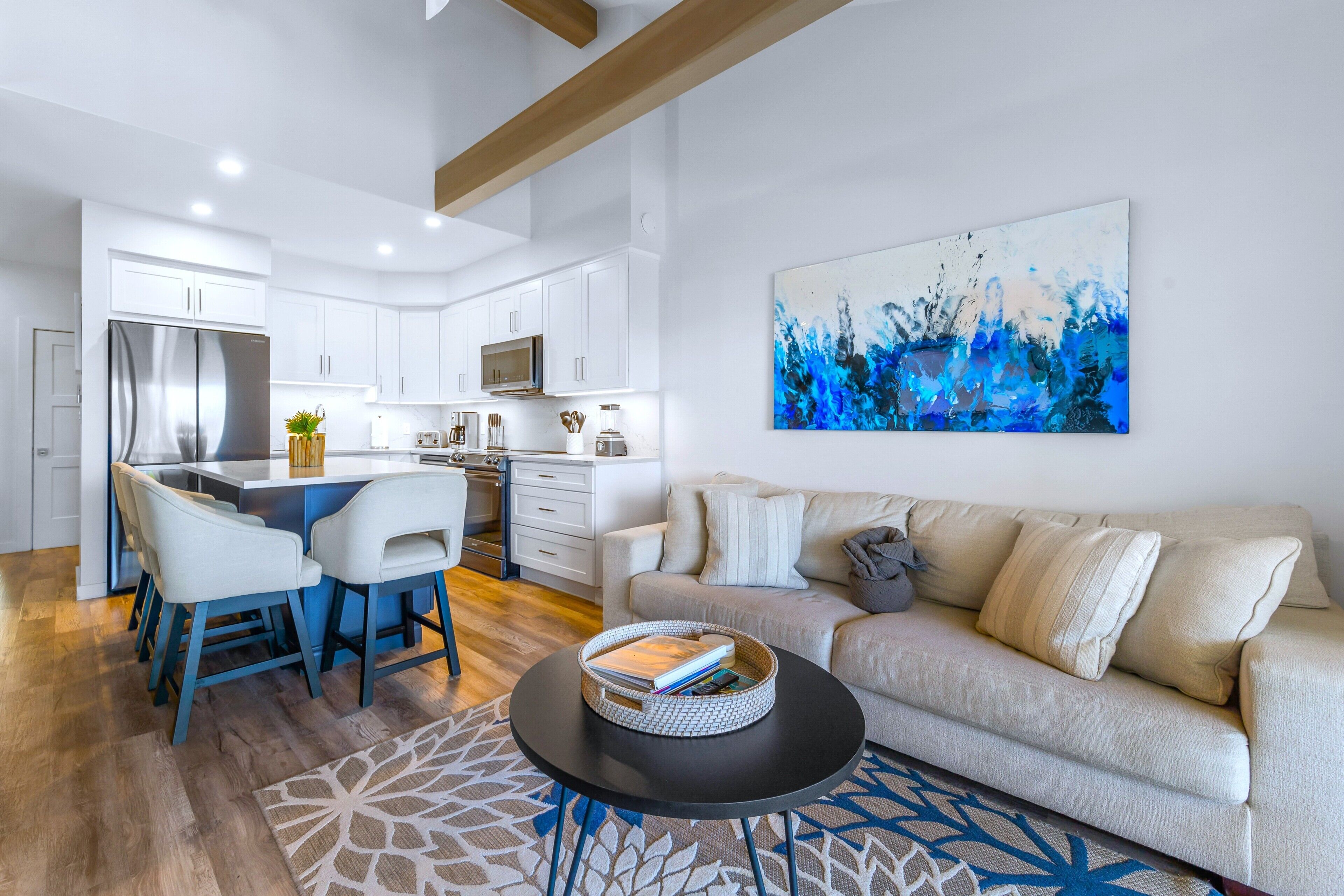 A modern kitchen with white cabinets, a stainless steel refrigerator, and a dining area with chairs and a table.
