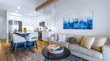A modern kitchen with white cabinets, a stainless steel refrigerator, and a dining area with chairs and a table.