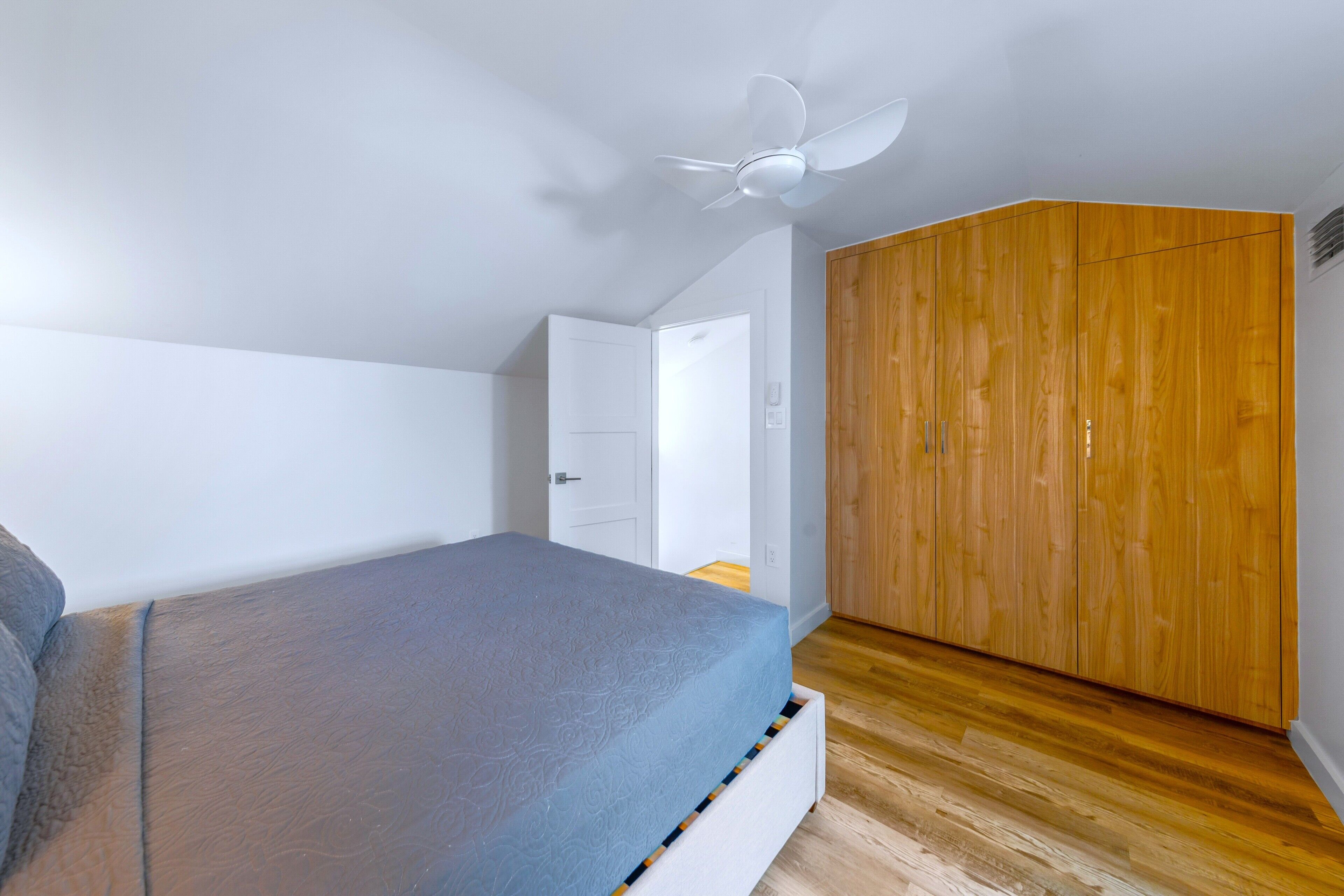 Un dormitorio con cama, armario de madera, ventilador de techo y puerta blanca.