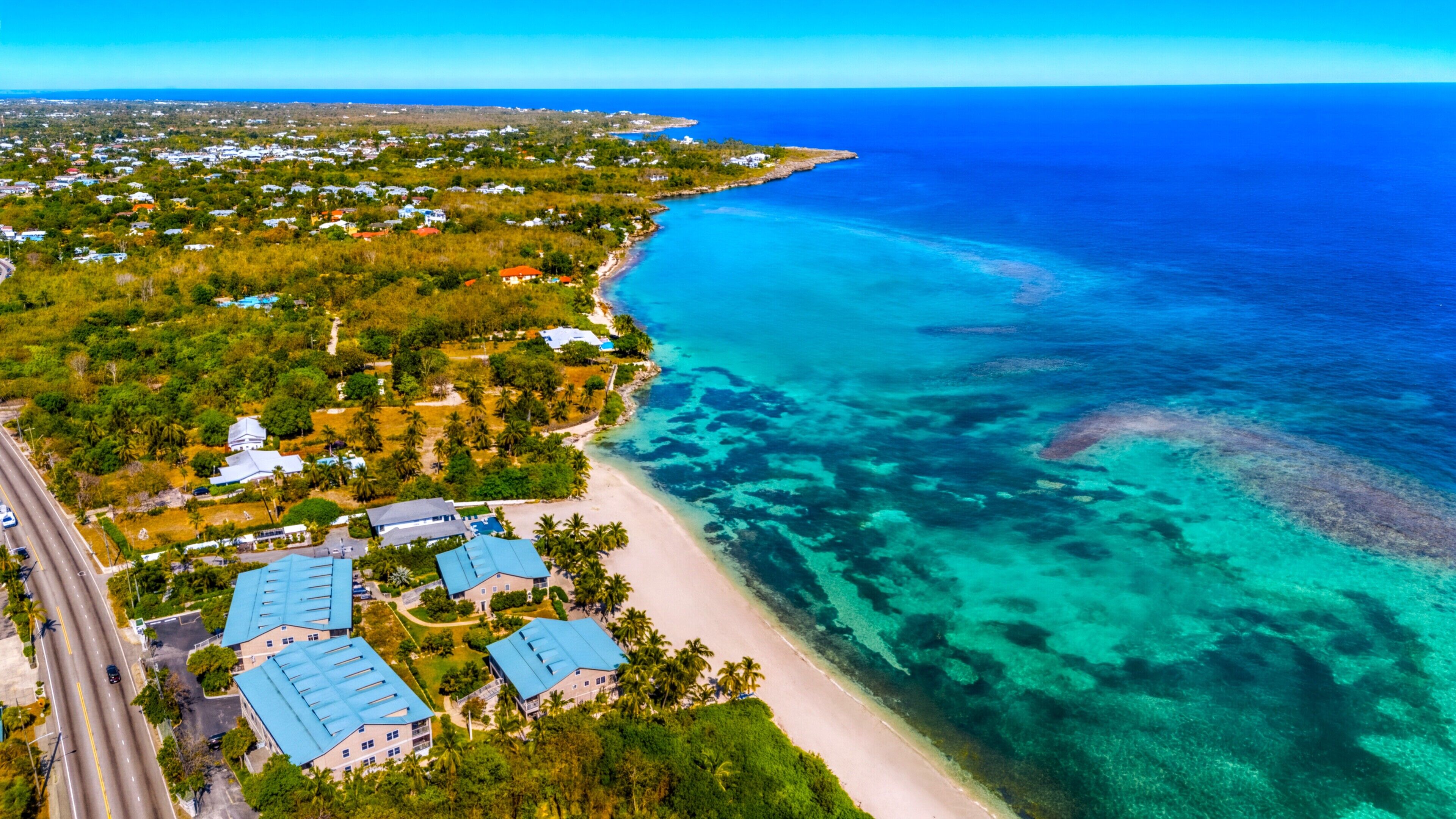 Vue aérienne d’une zone côtière avec une plage, des eaux d’un bleu limpide et des immeubles résidentiels aux toits bleus.